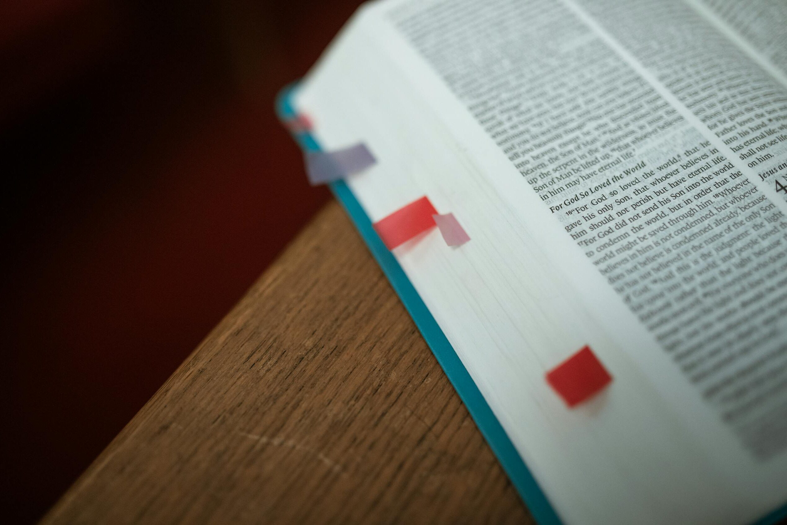 Close-up of an open Bible with colorful bookmarks on a wooden desk.